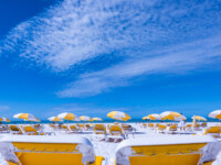 Sunny beach scene with yellow umbrellas and lounge chairs under a clear blue sky.
