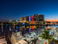 Night view of a vibrant waterfront city with illuminated buildings and docked boats.