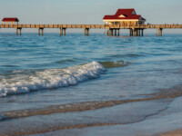 Pier with a red-roofed building extending over calm ocean waters.