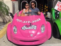 Two people enjoying a ride in a bright pink toy car.