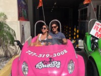 Two people enjoying a ride in a bright pink toy car.