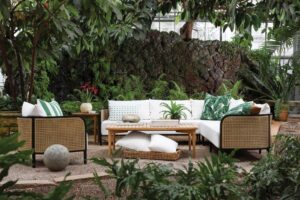 Cozy outdoor seating area with white cushions and wooden furniture surrounded by lush greenery.