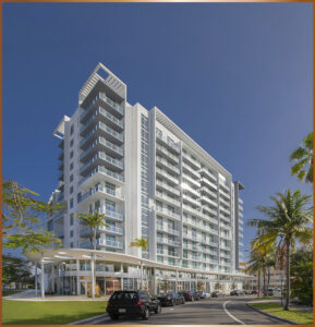 Modern glass and concrete high-rise building with balconies under a clear blue sky.