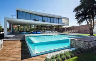 Modern house with a clear glass swimming pool and patio.