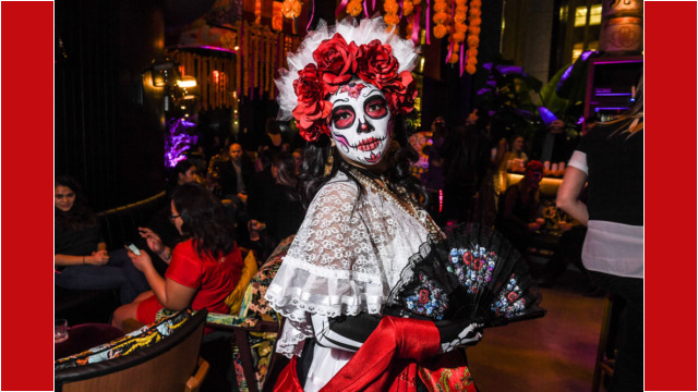 Person dressed in Day of the Dead costume with red flowers and face paint.