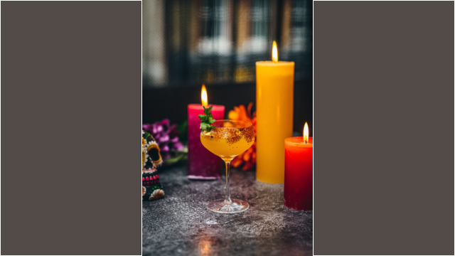 A cocktail glass with cinnamon sticks surrounded by colorful candles and festive decorations.