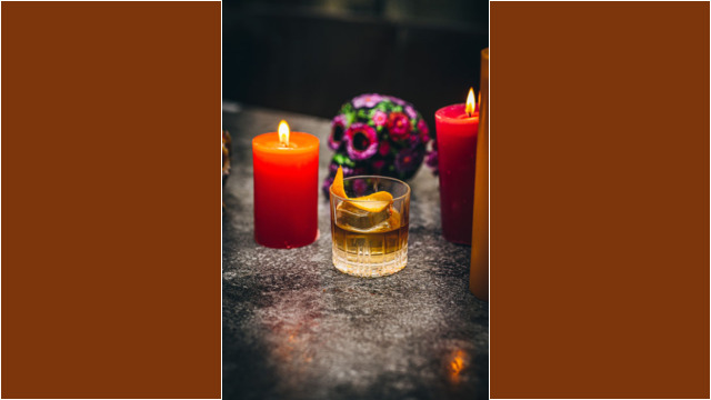 A glass of whiskey with lemon and three lit candles.