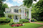 Historic house with white columns and American flag, surrounded by greenery.