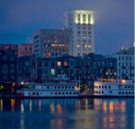 Two illuminated boats docked by city buildings at dusk.