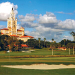 Golf course with clubhouse under a blue sky and clouds.