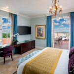 Elegant hotel room with a balcony overlooking the sea and cityscape.