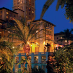 A warmly lit building surrounded by palm trees at twilight.