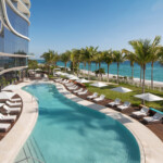 Luxury poolside view with palm trees and ocean in the background.