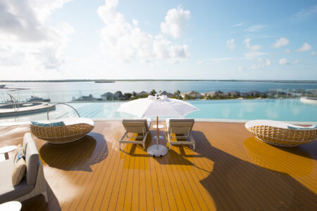 Sunlit poolside lounge with ocean view under a bright sky.