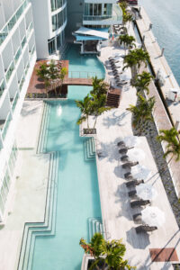 Aerial view of a modern outdoor pool with lounge chairs and palm trees.