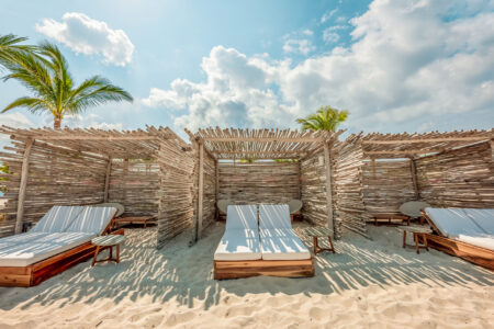 A cozy beach cabana with a double lounge bed under a clear blue sky.