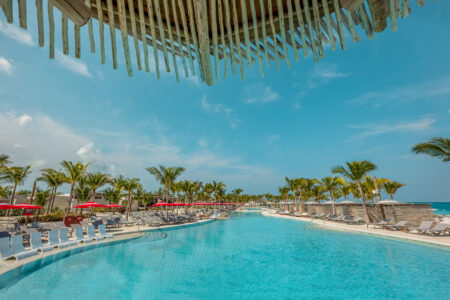 A large resort pool under a clear blue sky with palm trees.