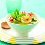 Shrimp and vegetable soup garnished with fresh basil in a green bowl.