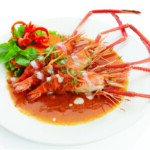 Plate of cooked shrimp in spicy sauce garnished with greens.