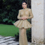 Woman in an elegant gold gown with a peplum detail posing outdoors.