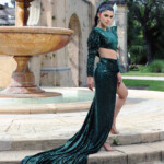 Woman in elegant green velvet dress with long train by fountain.