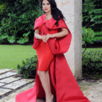 Woman in elegant red gown posing outdoors with matching accessories.