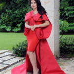 Woman in elegant red gown posing outdoors with matching accessories.
