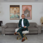 Man in a green blazer sitting confidently on a white chair in a modern living room.