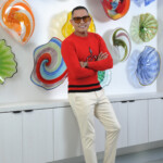 Man in red sweater posing in front of colorful glass art.