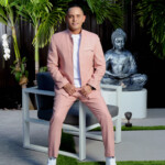 Man in a stylish pink suit sitting on a chair outdoors.