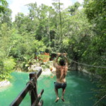 A person jumping into a natural pool surrounded by lush greenery.