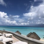 Beachfront lounge chairs under a cloudy sky by turquoise waters.
