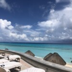 Beachfront lounge chairs under a cloudy sky by turquoise waters.