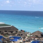 Beach resort with blue umbrellas and thatched roofs by the ocean.