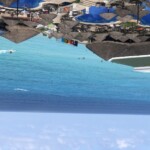 Beach resort with blue umbrellas and thatched roofs by the ocean.