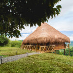 A thatched-roof hut surrounded by greenery under a cloudy sky.