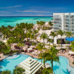 A tropical resort with a pool, palm trees, and beachfront views.