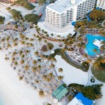 Aerial view of a beachfront resort with pools and palm trees.
