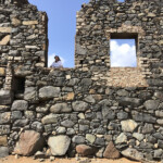 Person peeking through stone wall windows under clear sky.