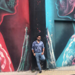 Man standing against colorful urban mural with contrasting red and blue faces.
