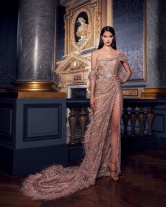 Model in an elegant, intricately beaded gown with a long train in a grand room.
