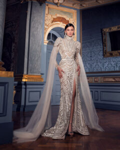 Elegant woman in an embellished gown with a long cape in a grand room.