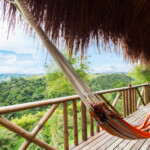 Hammock on a wooden balcony overlooking lush green forest.