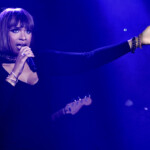 Female singer performing on stage with a microphone under blue lighting.