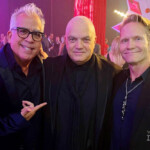 Three men posing together at an event with red lighting.