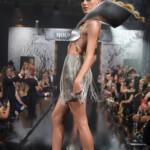 Model walks the runway in a silver dress at a fashion show.
