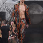 Model wearing a bold orange and black patterned suit on runway.