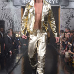Model walking runway in shiny gold jacket and pants.