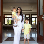 A woman holding a child and standing next to a boy at a doorway.