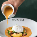 Pouring creamy soup into a bowl labeled Zucca with garnish and cream.